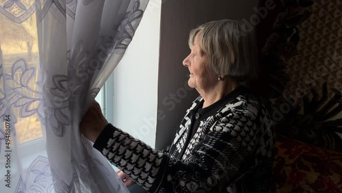 An old woman looks out the window of a rural house in Ternopil region, Ukraine
