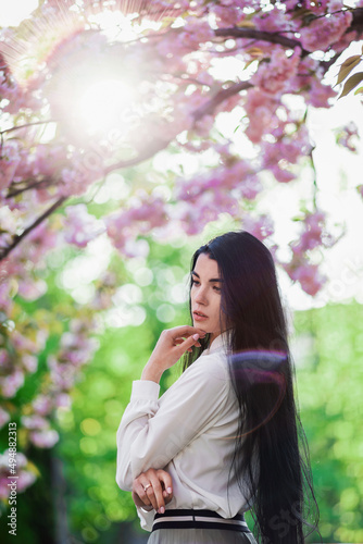 Young brunette posing near cherry blossoms in the park. Spring mood