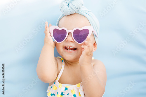 Funny cute baby girl on summer vacation. Child having fun in swimming pool. Sweet toddler girl in colorful swimsuit and sunglasses relaxing on sunbed. Free space for text.
