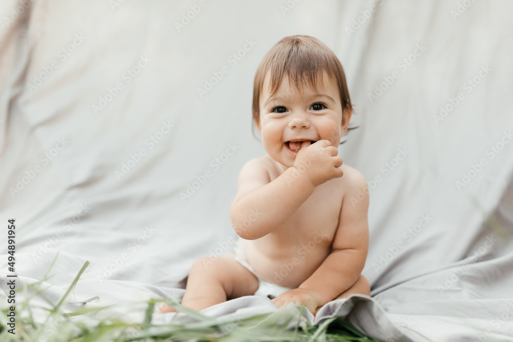 A baby in a diaper sits on the street on a gray background, laughs and looks at the camera A baby in a diaper sits on the street on a gray background, laughs and looks at the camera