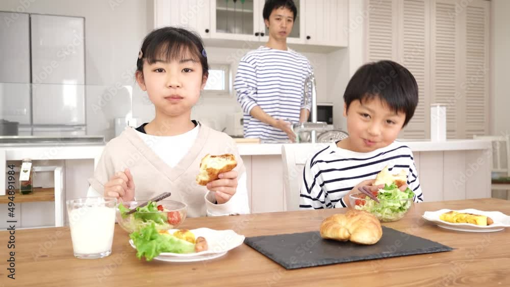 朝食でパンを食べる子供と洗い物をする父親 朝食でパンを食べる子供と洗い物をする父親