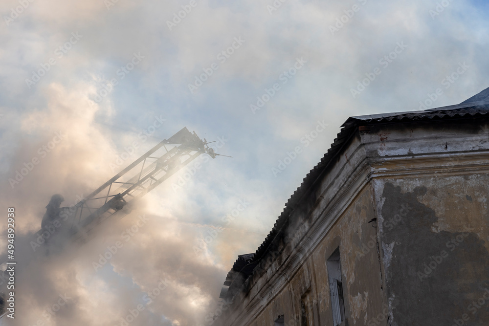 Firefighter pours water on fire. Rescue services during work. Extinguishing fire from hydrant. Firefighter on retractable ladder.