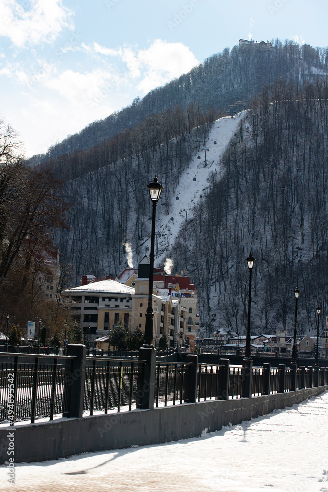 Fototapeta premium Sochi, Russian Federation - March 17, 2022: The view of the town hall Rosa Khutor, and Mzymta river with cabins of a cable car. Krasnaya Polyana.