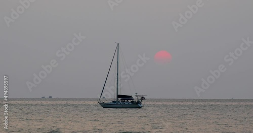 Beautiful Sunset with a Large Sun Going Down Behind a Yacht on the Horizon in Bangsaray near Pattaya, Thailand. Stationary Zoomed Shot in 4K. photo