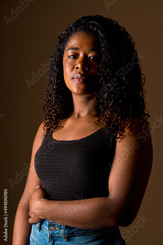 Mid waist portrait of african american woman with dark hair and casual clothes. Vertical side view of african woman with sad expression in brown background. People diversity concept.