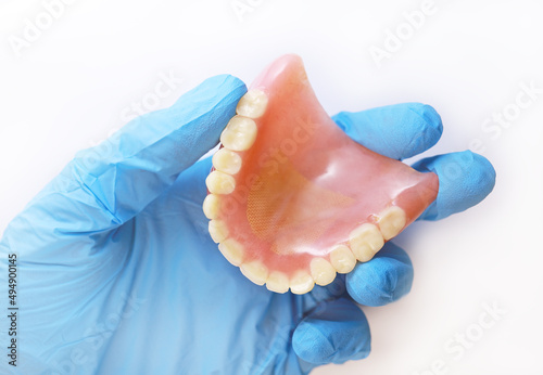 Used acrylic denture in a gloved hand. Doctor's hand holds a denture. Set of false teeth.