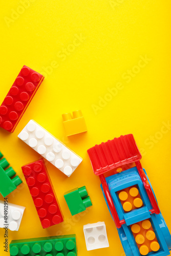 Multicolored blocks of the children s constructor lie on a yellow background. Vertical photo.