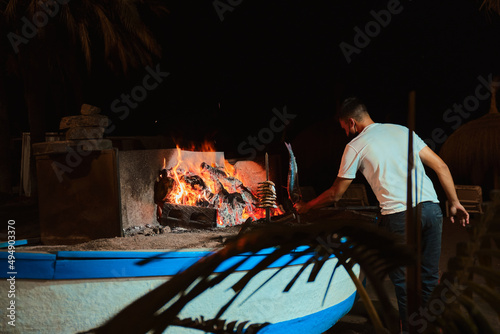 Barbecue on a boat on the beach of Malaga with a young waiter cooking a brochette of sardines, at night