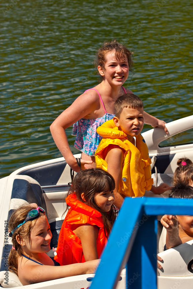 Children rest on a motor boat. Boys and girls are sitting in a speedboat. Active recreation on the water in summer.