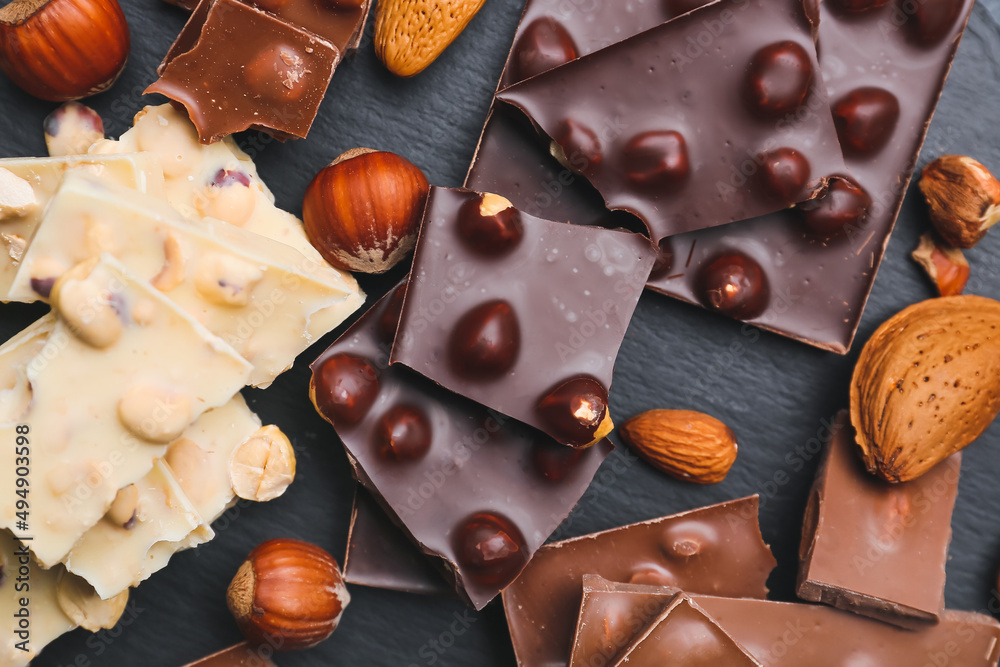 Pieces of tasty chocolate with nuts on dark background