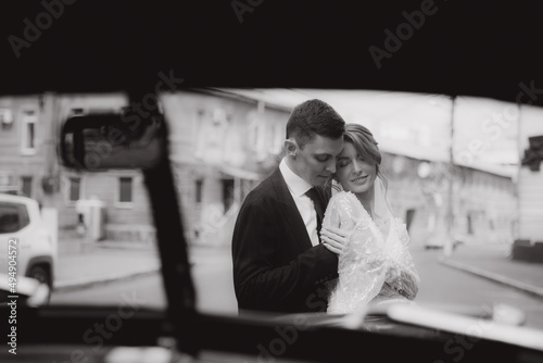 Wedding of a beautiful, stylish couple, a bride in a white wedding dress and a groom in a black suit, tuxedo, in a black retro car.