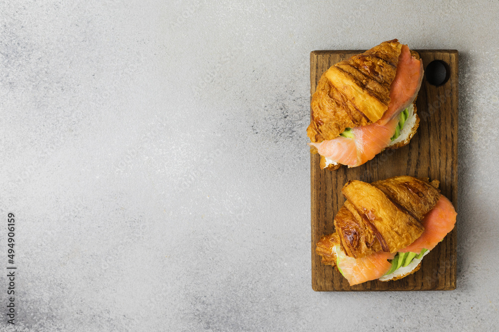 2 croissant with salmon, avocado and cream cheese on a wooden board on a gray background, top view 2 croissant with salmon, avocado and cream cheese on a wooden board on a gray background, top view