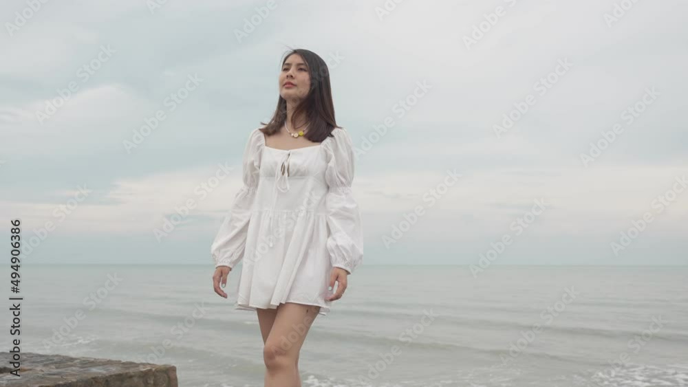 Lonely beautiful young asian woman in white dress walking on boardwalk in tropical sea on overcast Lonely beautiful young asian woman in white dress walking on boardwalk in tropical sea on overcast