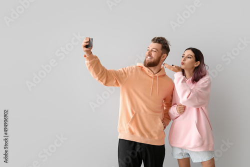 Cool young couple in hoodies taking selfie on light background photo