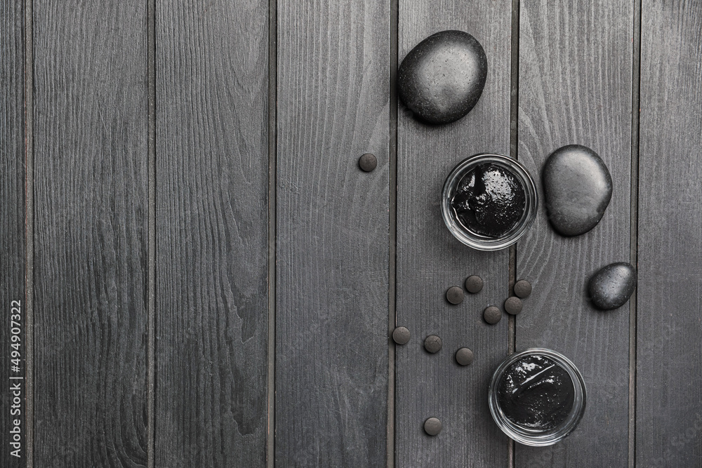 Bowls of activated carbon facial mask, pills and spa stones on dark wooden background Bowls of activated carbon facial mask, pills and spa stones on dark wooden background