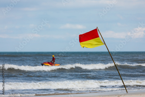 red and yellow flag on the beach with a lifeguard on a jet ski