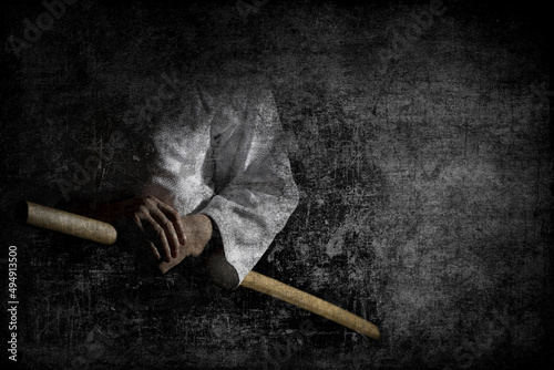 Person in black hakama standing in fighting pose with wooden sword bokken over dark grunge background.