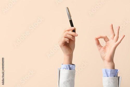 Businesswoman with pen showing OK on beige background