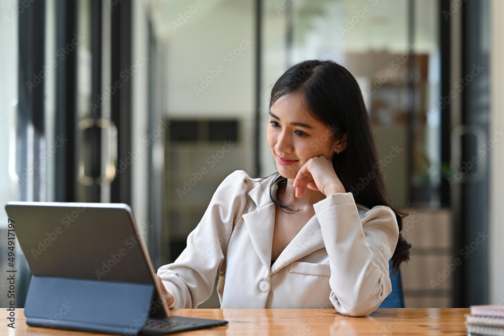 A portrait of a pretty Asian woman sitting in the office looking at a tablet and working on a document, for business and technology concept. A portrait of a pretty Asian woman sitting in the office looking at a tablet and working on a document, for business and technology concept.