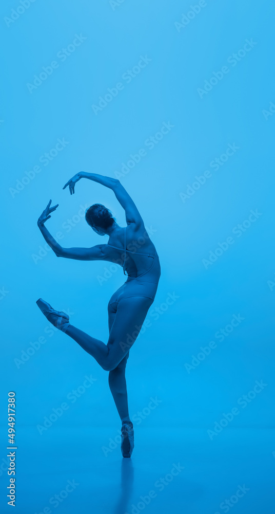 Grace. Young and graceful ballet dancer isolated on blue studio background in neon light. Art, flexibility, inspiration concept.