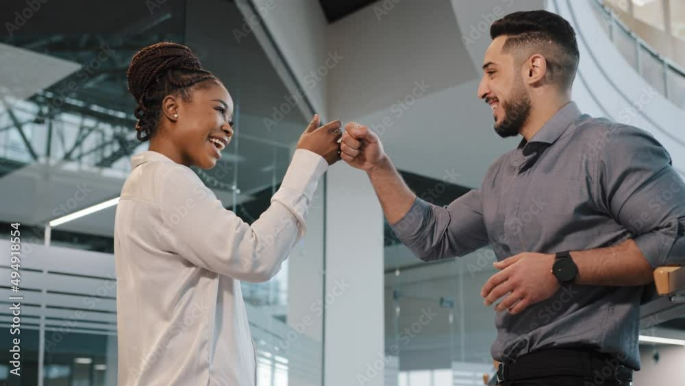 Two coworkers friendly diverse business partners colleagues african woman with arabian indian man employee talking in office partnership teamwork gesture make blow with fists support unity symbol Two coworkers friendly diverse business partners colleagues african woman with arabian indian man employee talking in office partnership teamwork gesture make blow with fists support unity symbol