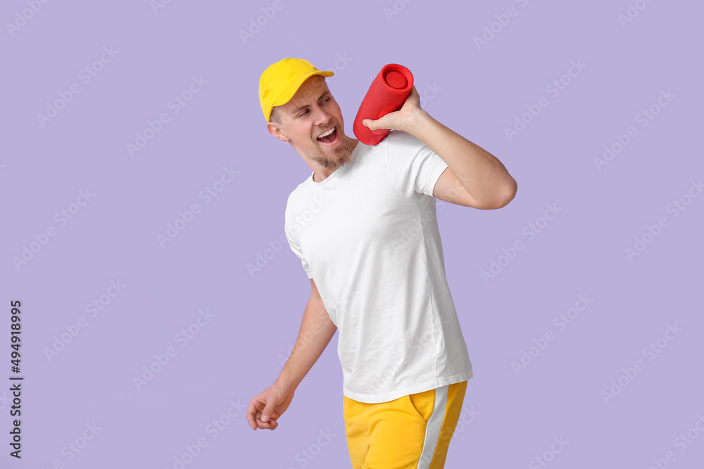 Emotional man with wireless portable speaker on violet background