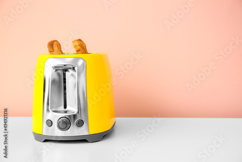 Modern toaster with bread slices on table