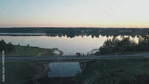 Young people on a lonely road on a bridge near a church and river on a foggy morning at dawn. River, forest, fog, village