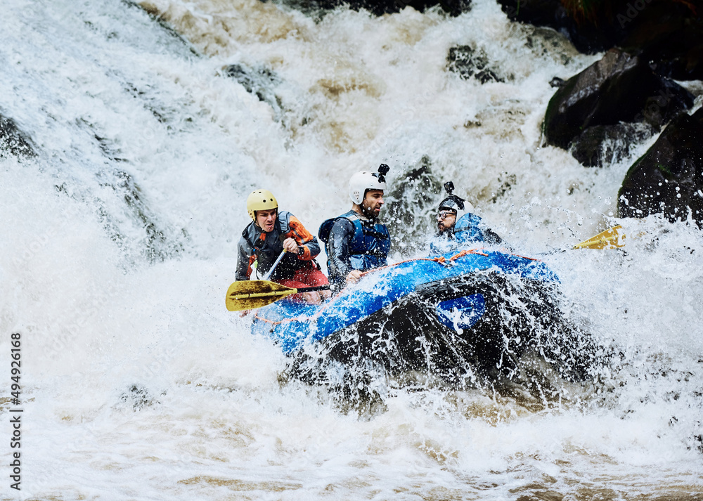 We asked for extreme adventure and we got it. Shot of a group of determined young men on a rubber boat busy paddling on strong river rapids outside during the day.
