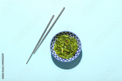 Bowl with healthy seaweed salad on blue background