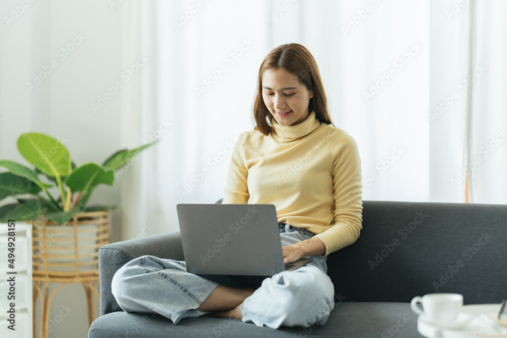 Smiling beautiful young asian ethnicity woman sitting on sofa with computer on lap, thinking of daily work, planning freelance working schedule, dreaming of vacation or visualizing alone at home. Smiling beautiful young asian ethnicity woman sitting on sofa with computer on lap, thinking of daily work, planning freelance working schedule, dreaming of vacation or visualizing alone at home.
