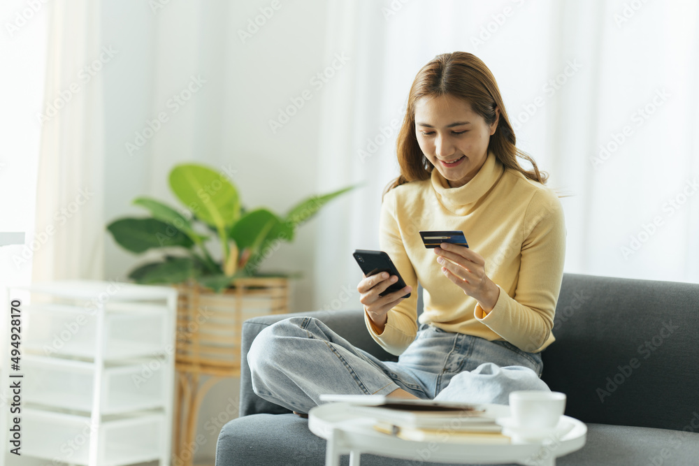 Online shopping concept. Dreamy asian woman with smartphone and credit card sitting on couch, thinking about internet purchases or food delivery, free space Online shopping concept. Dreamy asian woman with smartphone and credit card sitting on couch, thinking about internet purchases or food delivery, free space