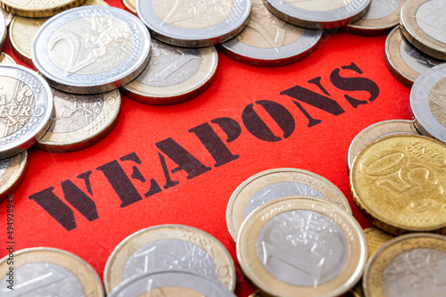 Text "weapons" in black, on a red surface, and coins around it. Arms trade and wealth generated. 