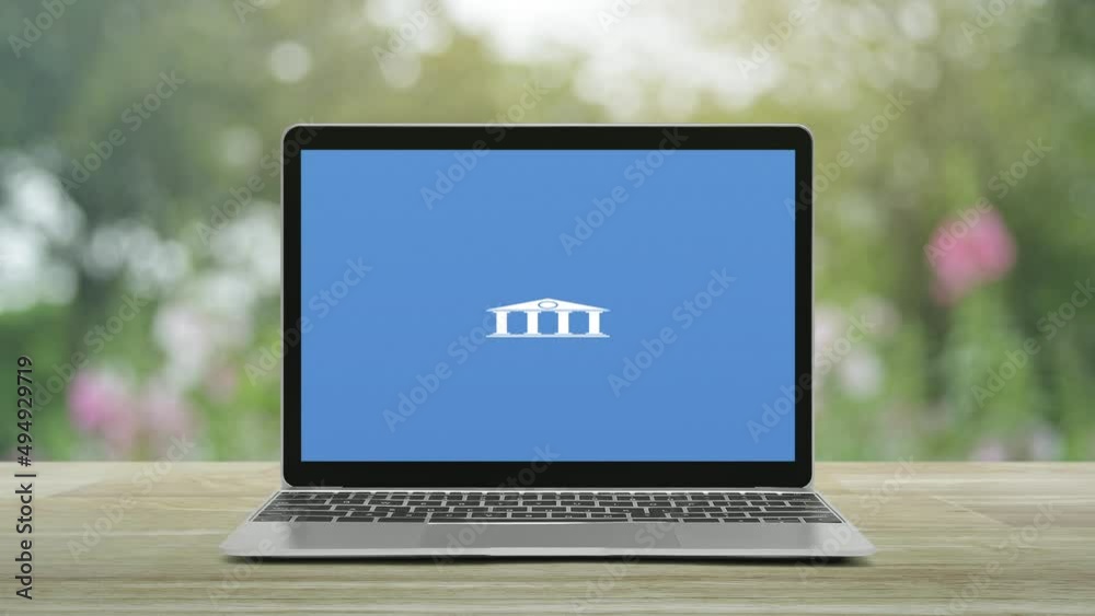 Bank flat icon on modern laptop computer monitor screen on wooden table over blur pink flower and tree in park, Business banking online concept Bank flat icon on modern laptop computer monitor screen on wooden table over blur pink flower and tree in park, Business banking online concept
