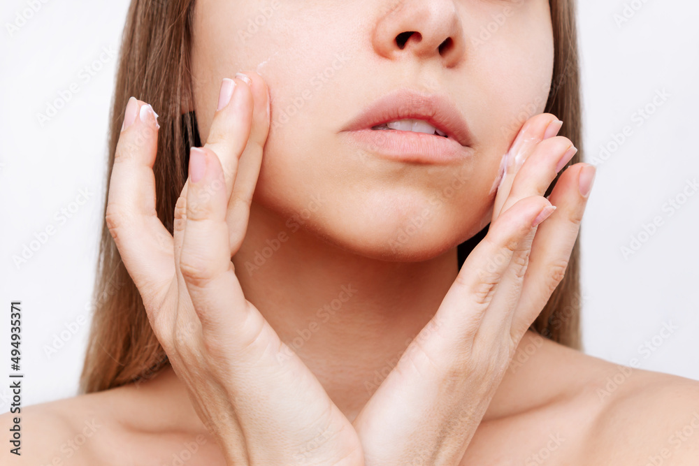 Cropped shot of a young attractive caucasian blonde woman touching the face with her hand applying a moisturizing cream on the skin isolated on a white background. Cosmetology and beauty concept Cropped shot of a young attractive caucasian blonde woman touching the face with her hand applying a moisturizing cream on the skin isolated on a white background. Cosmetology and beauty concept