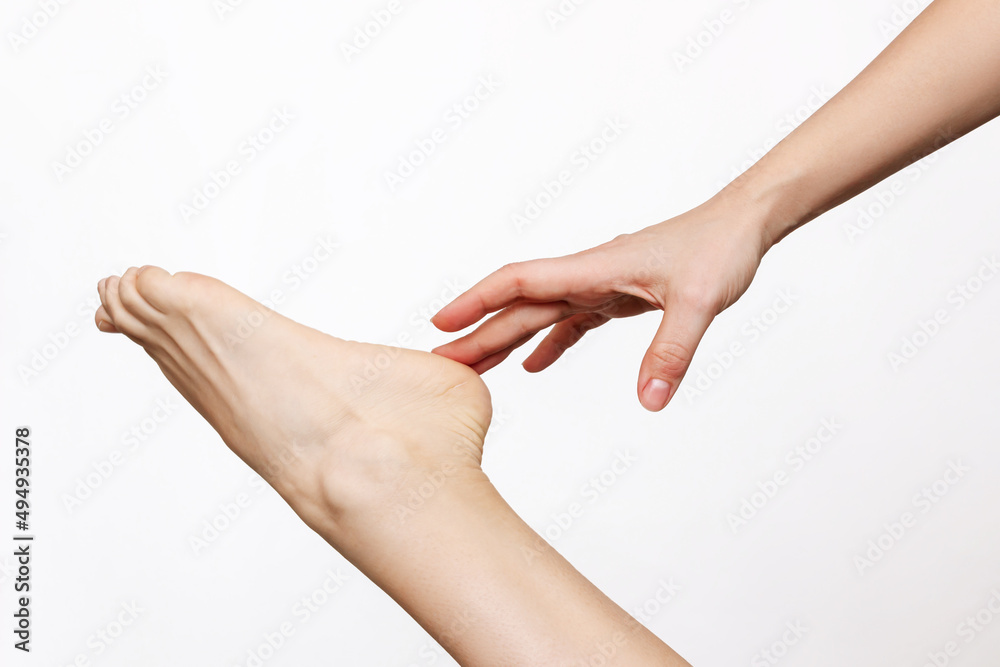 Cropped shot of a young woman touching the heel with her hand. The girl moisturizing the dry cracked foot with a cream for skin softness isolated on a white background. Skin care concept