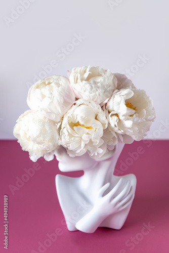 Fresh bunch of white peonies in vase in shape of womens face on dusty pink background. Trendy Ceramic Vase of human head, Handmade Modern Statue Art Flower Vase. Card Concept, copy space for text