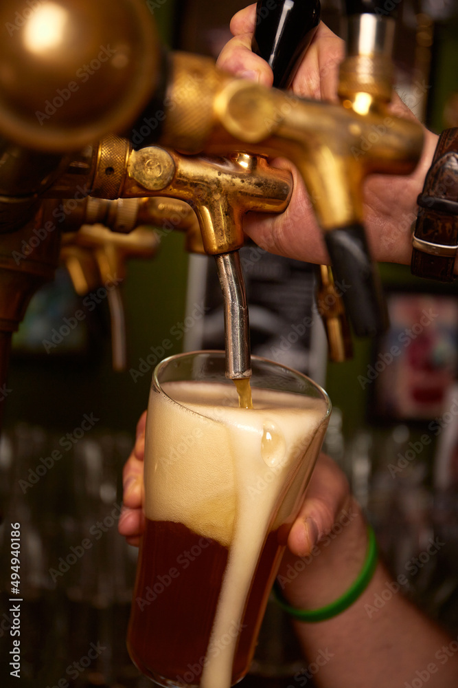 Obraz premium Hand bartender pouring large lager beer. Light cold filtered beer in glass beaker.