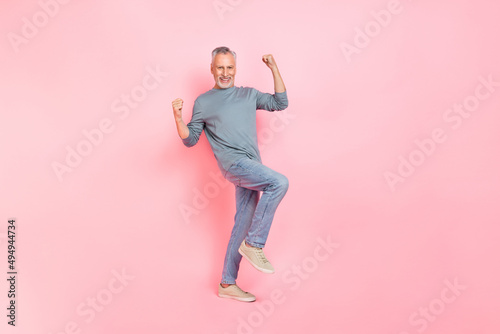 Photo of lucky charming man pensioner dressed grey shirt walking rising fists isolated pink color background