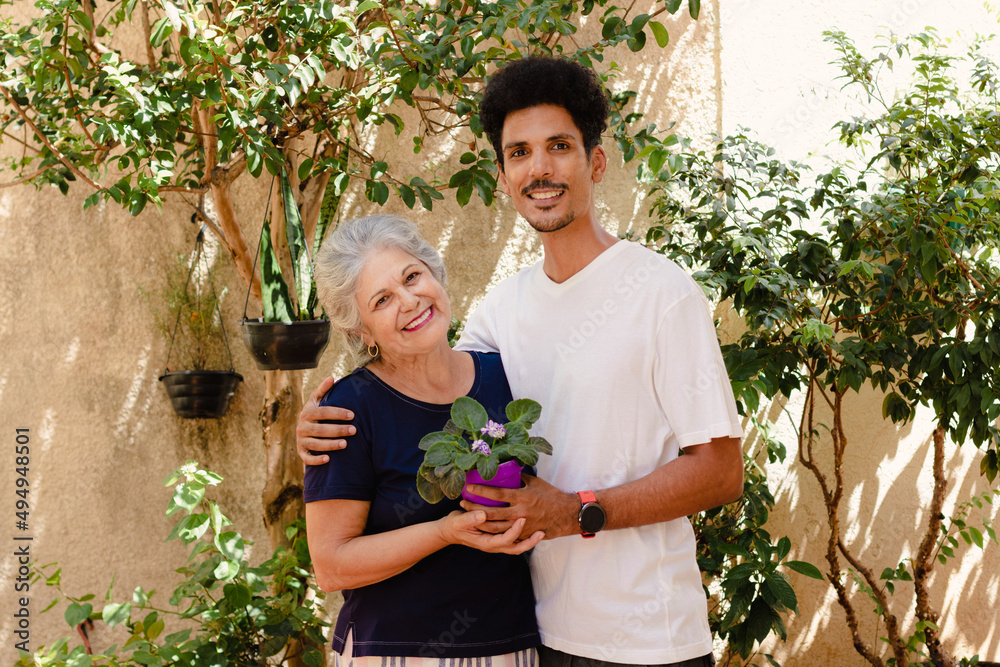 Mother's Day. Caucasian mother receives flowers from her black son in the garden at home.