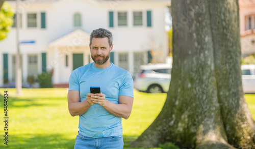 smiling mature man standing outdoor at house chatting on phone, buy online