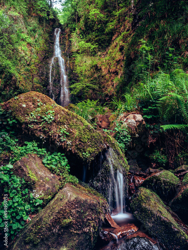 Vertical shot of spectacular Belaustegi waterfall in green forest in Spain photo