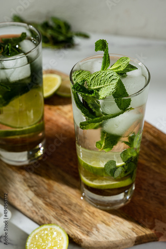 Non-alcoholic mojitos with ice, mint and lime slices on wooden board. Refreshing summer cocktails.