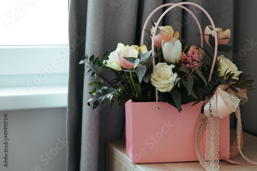 Bouquet of fresh flowers (roses, tulips, greens)  is on the bedside table by the window. The concept of a holiday, wedding, engagement, valentine's day, women's day, birthday or other events. 