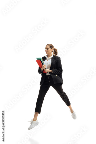 Dynamic portrait of young businesswoman in black suit holding folders, in motion isolated over white studio background