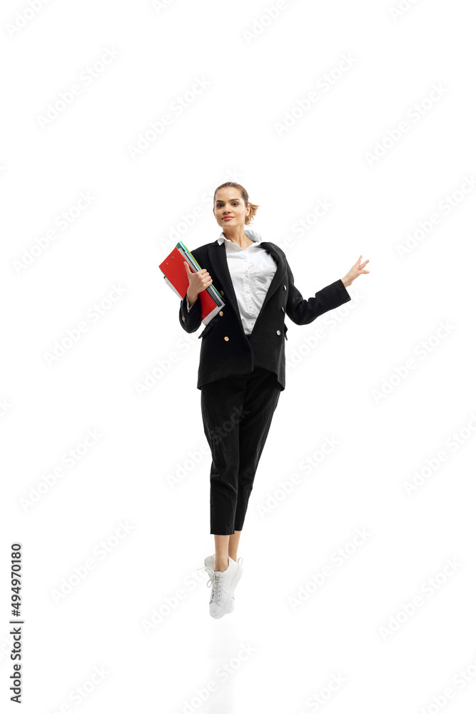 Dynamic portrait of young businesswoman in black suit jumping with folders isolated over white studio background Dynamic portrait of young businesswoman in black suit jumping with folders isolated over white studio background