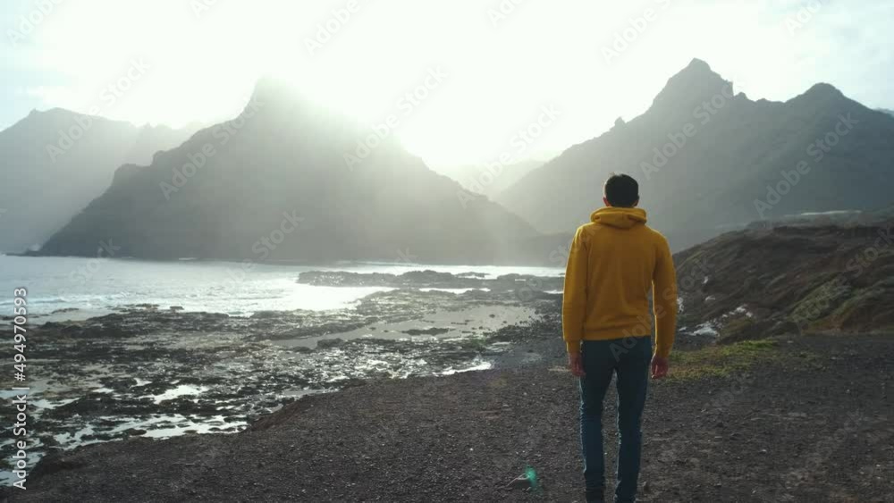 Tourist man in yellow sweatshirt walks on volcanic beach in north of Canary Island, Tenerife