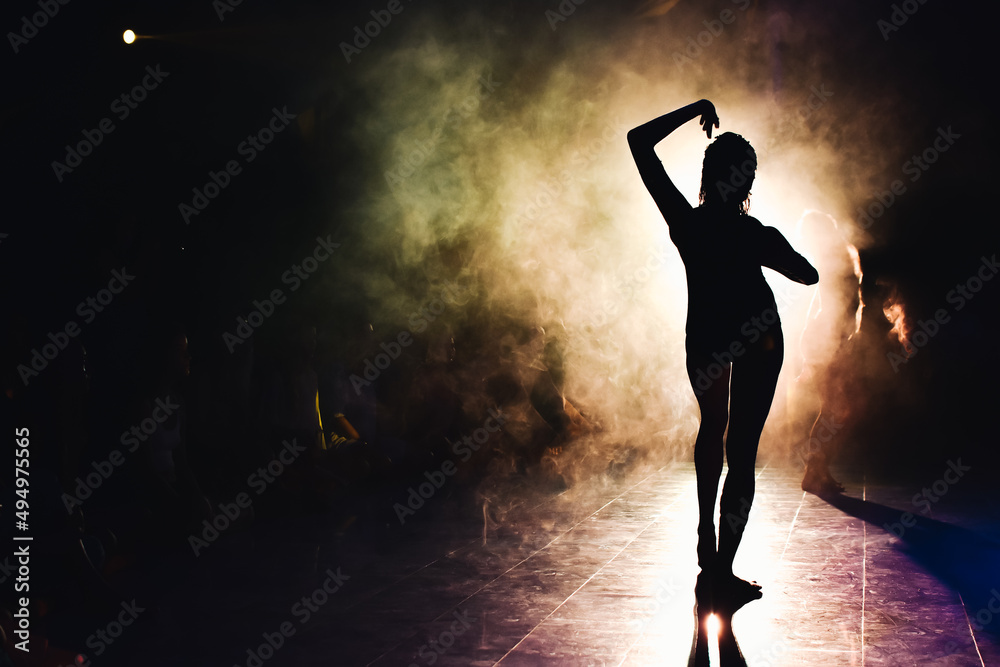 silhouette of a woman dancing between lights and smoke
