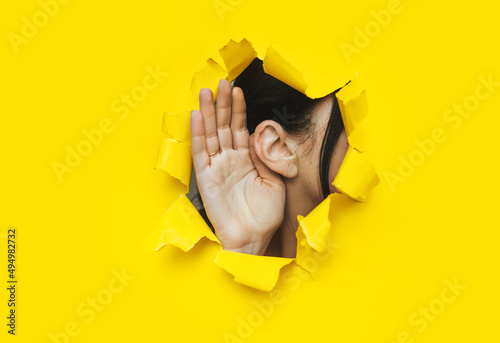 Foto Close-up of a woman's ear and hand through a torn hole in the paper