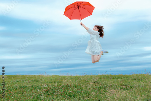草原で傘を持ってジャンプする女性